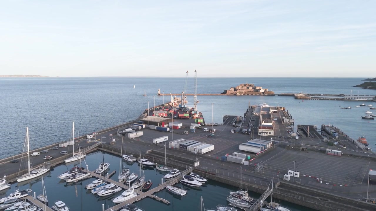 Puerto de St Peter Port, Guernsey, Islas del Canal. Metraje de dron revela el puerto, los concurridos muelles y el atraque de ferris, y la Marina QEII en North Beach con el Castillo Cornet al fondo bajo la luz del atardecer.
