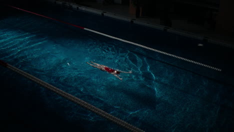 una mujer nadando en una piscina cubierta por la noche