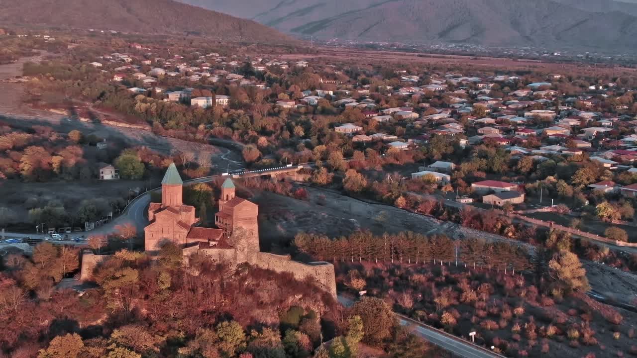 Sito storico in Georgia circondato da montagne e un villaggio sottostante.