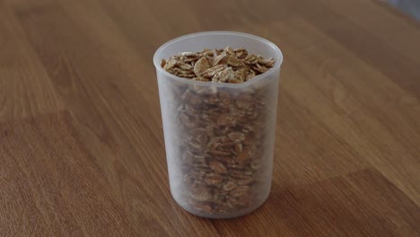 Pouring-oat-flakes-into-the-plastic-measurement-cup-container-on-the-wooden-table-in-the-kitchen