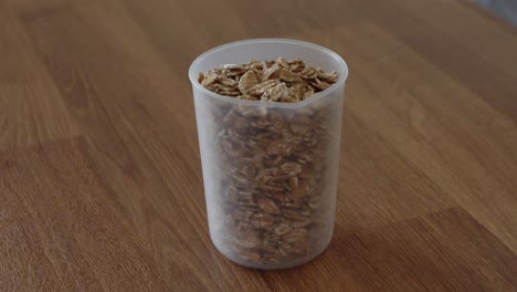 vertiendo copos de avena en el recipiente de taza de medición de plástico en la mesa de madera en la cocina