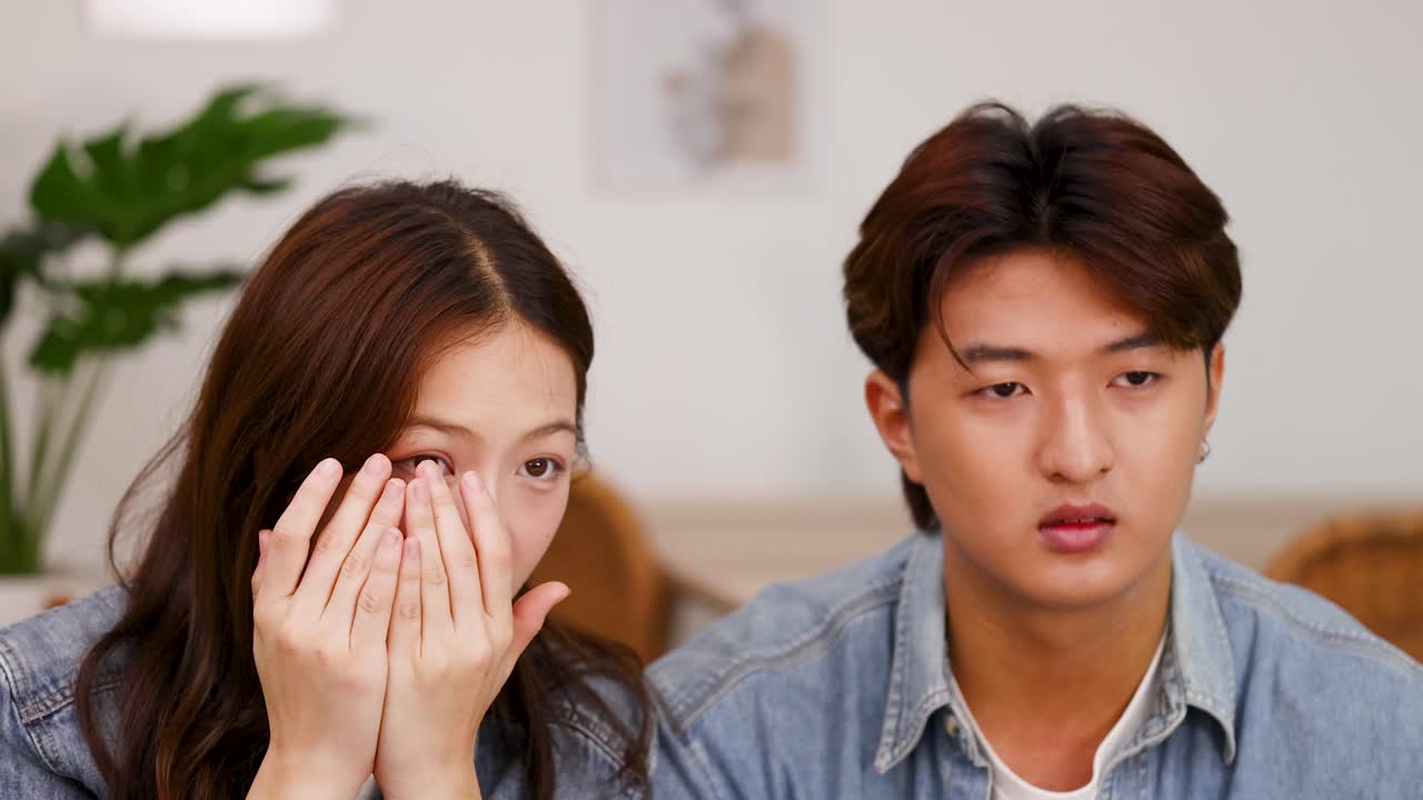 Asian couple on sofa reacting in fear and surprise to intense offscreen video content