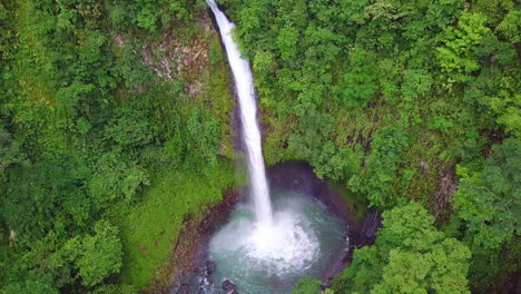 la fortuna waterfall crashing into turquoise pool in costa rica jungle, aerial pan