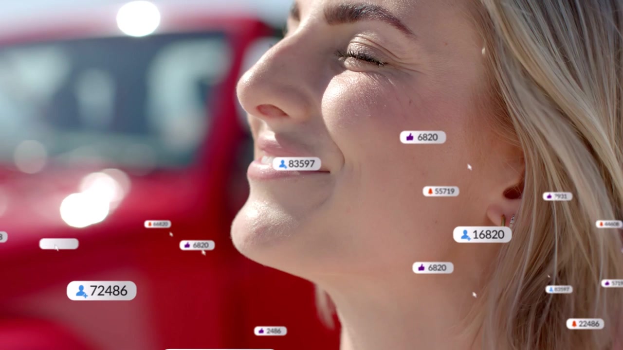 Adult woman touching face near red car, reacting to social media badges multiplying, smiling upward