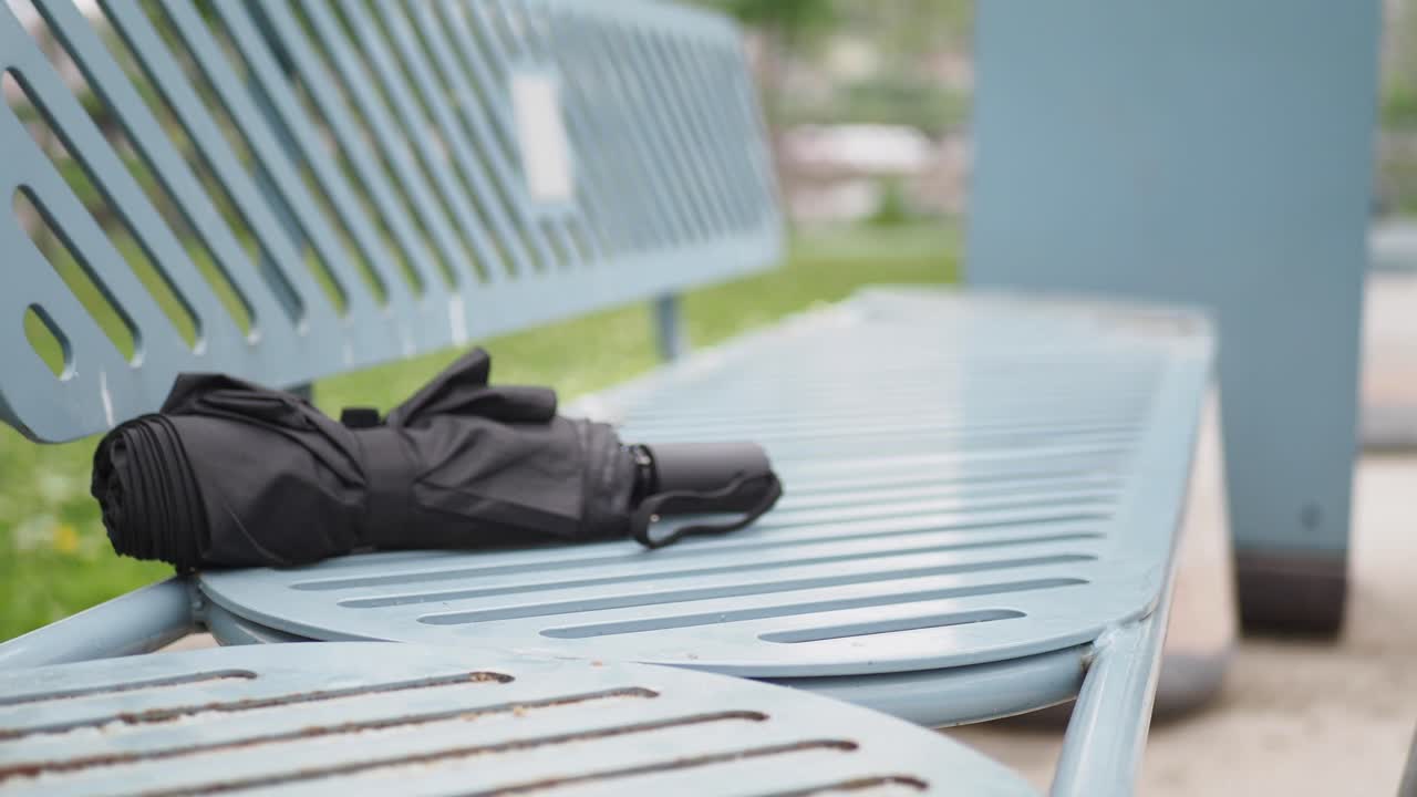 우산 을 들고 공원 벤치 에 갈색 크로스 보디 가방 을 들고 있는 여자