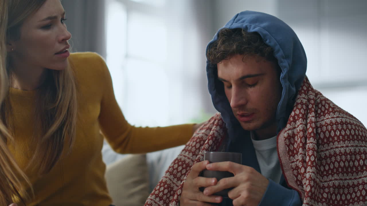 Concerned woman caring sick husband at home closeup. Guy drinking hot beverage