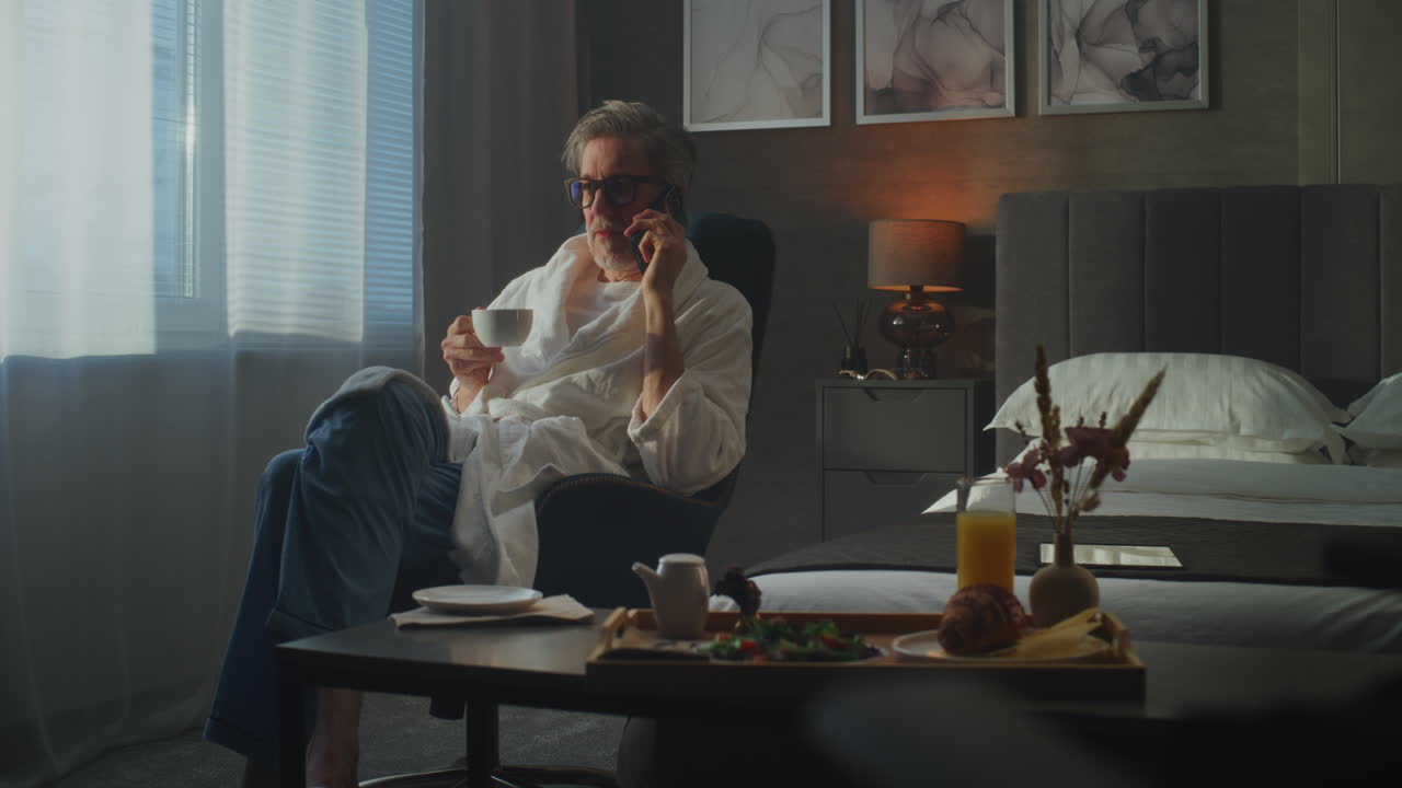 Man in a hotel room relaxing with coffee and a phone call