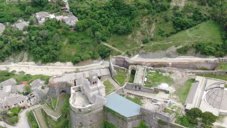 Drone-view-in-Albania-flying-in-Gjirokaster-town-over-a-medieval-castle-on-high-ground-fort-showing-the-brick-brown-roof-houses