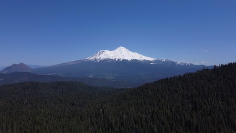 mount shasta from the forest in spring in california. contrast of blue sky, green trees, and white snow glaciers on the peak. shot in 4k focusing on the mountain towering over the valley.