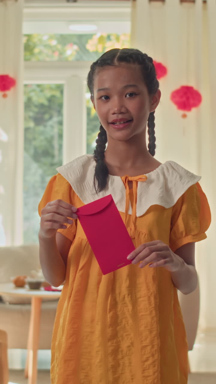 Cheerful Girl Demonstrating Tet Red Envelope for Tet to Camera