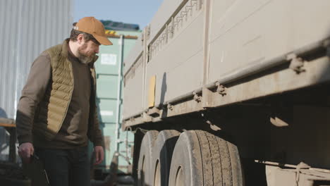 worker wearing vest and cap reading documents in a logistics park while walking