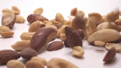 different nuts falling into pile on white background - close up, slow motion