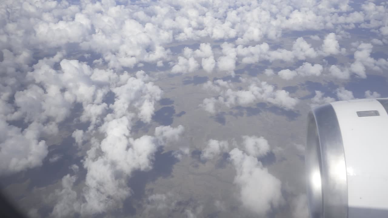 Powerful jet engine propelling commercial airliner soaring through pristine white clouds, revealing expansive ground landscape beneath bright blue sky