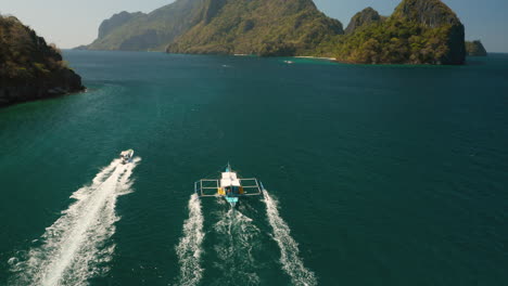 aerial tilt down showing speedboat and outrigger boat in el nido, palawan, pilippines