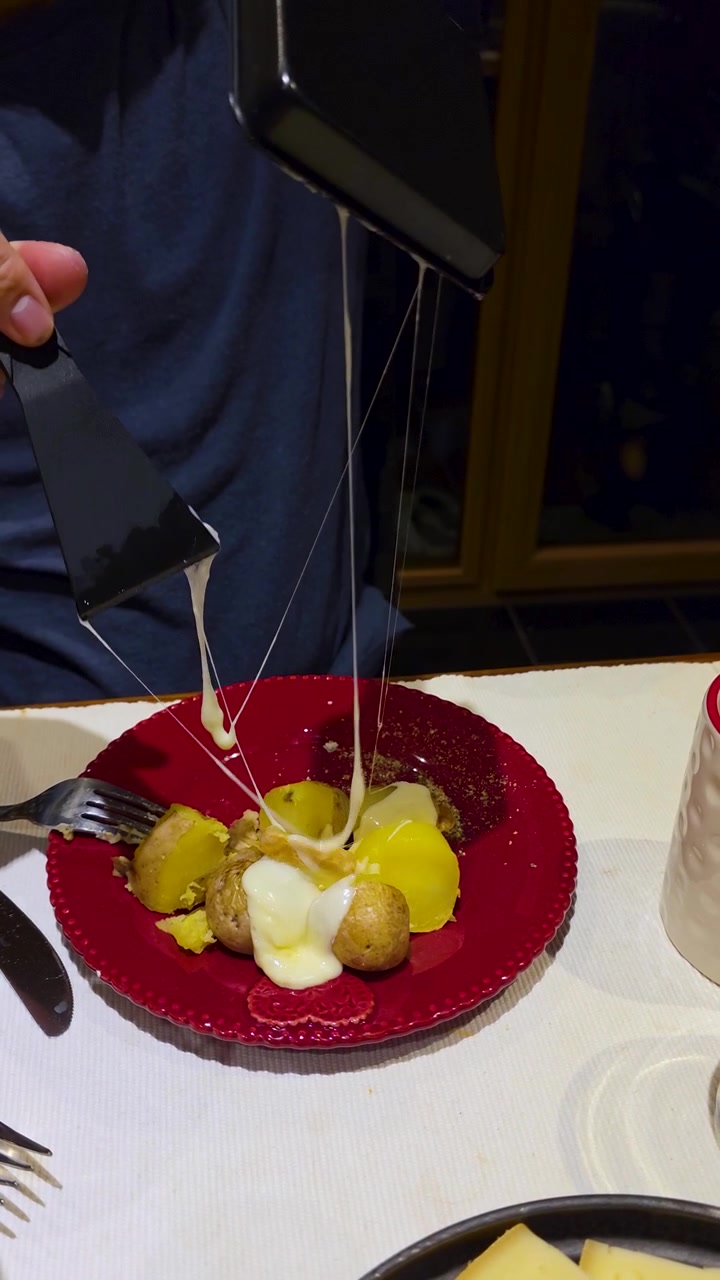 Tourist enjoying traditional Swiss raclette prepared on a tabletop grill, melting cheese over potatoes during an authentic alpine dining experience