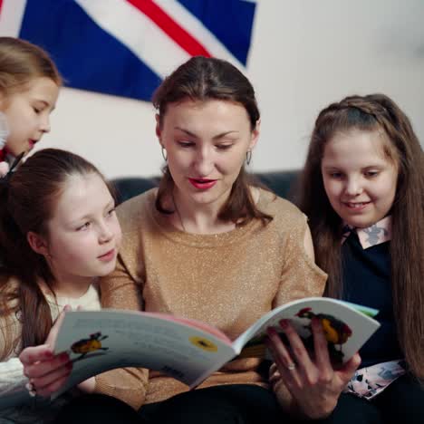 elementary education. woman teacher sitting together with little students on the couch and reading a book. schoolgirls talk with a teacher.