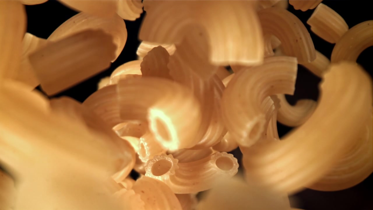 Pâtes macaroni sèches tombant au ralenti sur fond noir