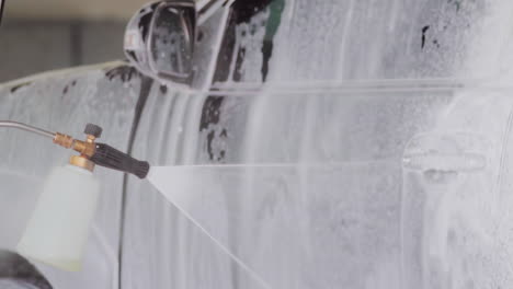 primer plano de una pistola de espuma de lavado de coches rociando espuma blanca en la ventana del coche