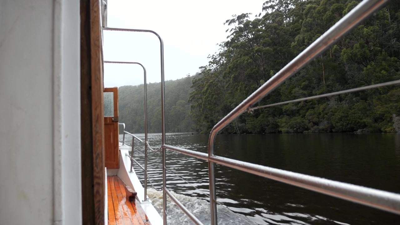 Seitenansicht eines alten Holzbootes auf einer Flussfahrt, stimmungsvolle und nieselige Umgebung. Zeitlupenaufnahme. Pieman River Cruise. Corinna, Tasmanien, Australien