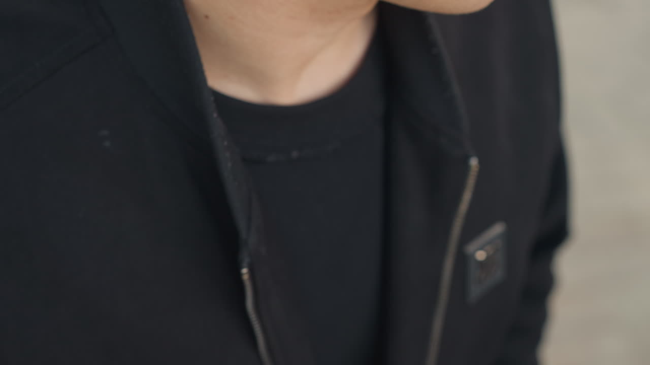 검은색 후드티 깃과 지퍼를 클로즈업해서 매만지는 젊은 남성, 손으로 옷감을 만지작거리고 손가락으로 소매와 깃을 잡아당김, 도시적인 캐주얼 의상, 미묘한 초조함, 오디션 준비 분위기, 질감