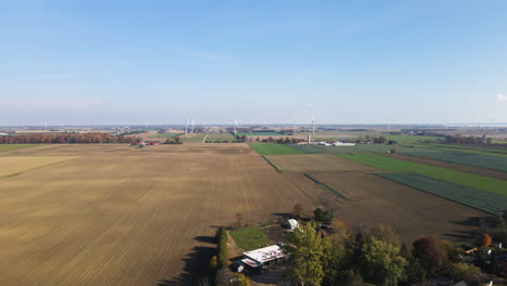 Drone-push-in-above-forested-farm-houses-with-large-crop-fields-and-cloud-shadows-on-land