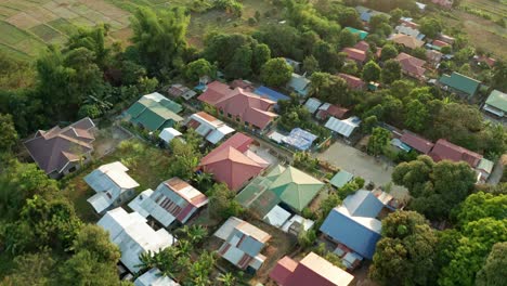 Vista-Aérea-De-Un-Pequeño-Pueblo-Moderno-Dentro-De-Un-Bosque-Al-Lado-De-Una-Granja-En-Filipinas-Durante-La-Puesta-De-Sol-De-La-Tarde-En-4k