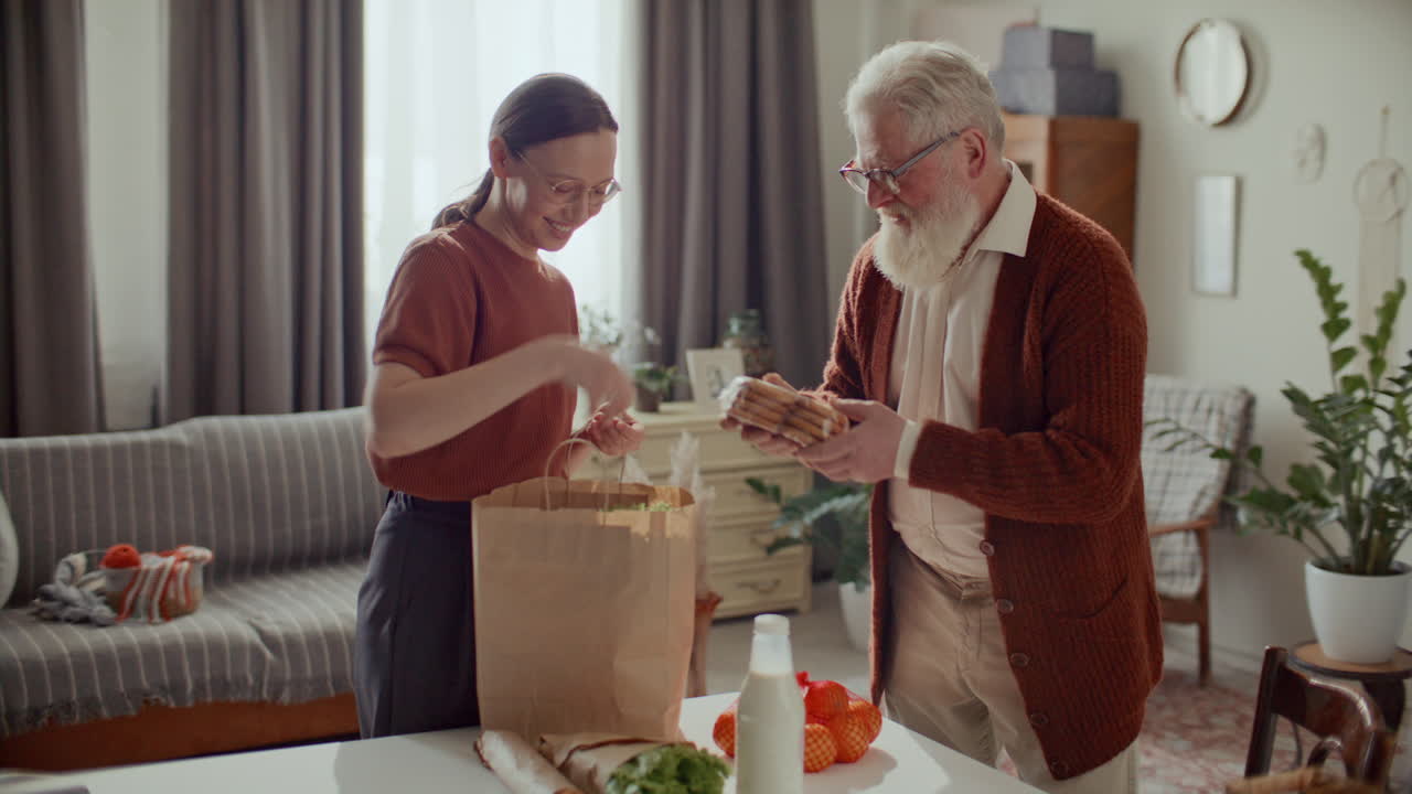 Young Woman Unpacking Groceries for Elderly Grandfather at Home