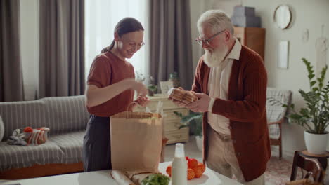young woman unpacking groceries for elderly grandfather at home