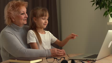 Beginning-of-online-school-classes,-greeting-the-teacher-using-a-video-call.-A-young-grandmother-and-granddaughter-study-on-a-laptop