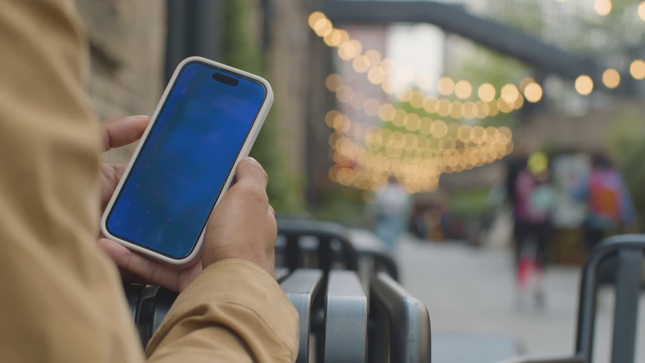 블루 스크린 휴대폰 1 을 보고 있는 무슬림 남성 이 도시 거리 에서 야외 에 앉아 있다