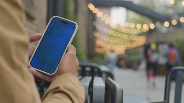 Close Up Of Muslim Man Sitting Outdoors On City Street Looking At Blue Screen Mobile Phone 1