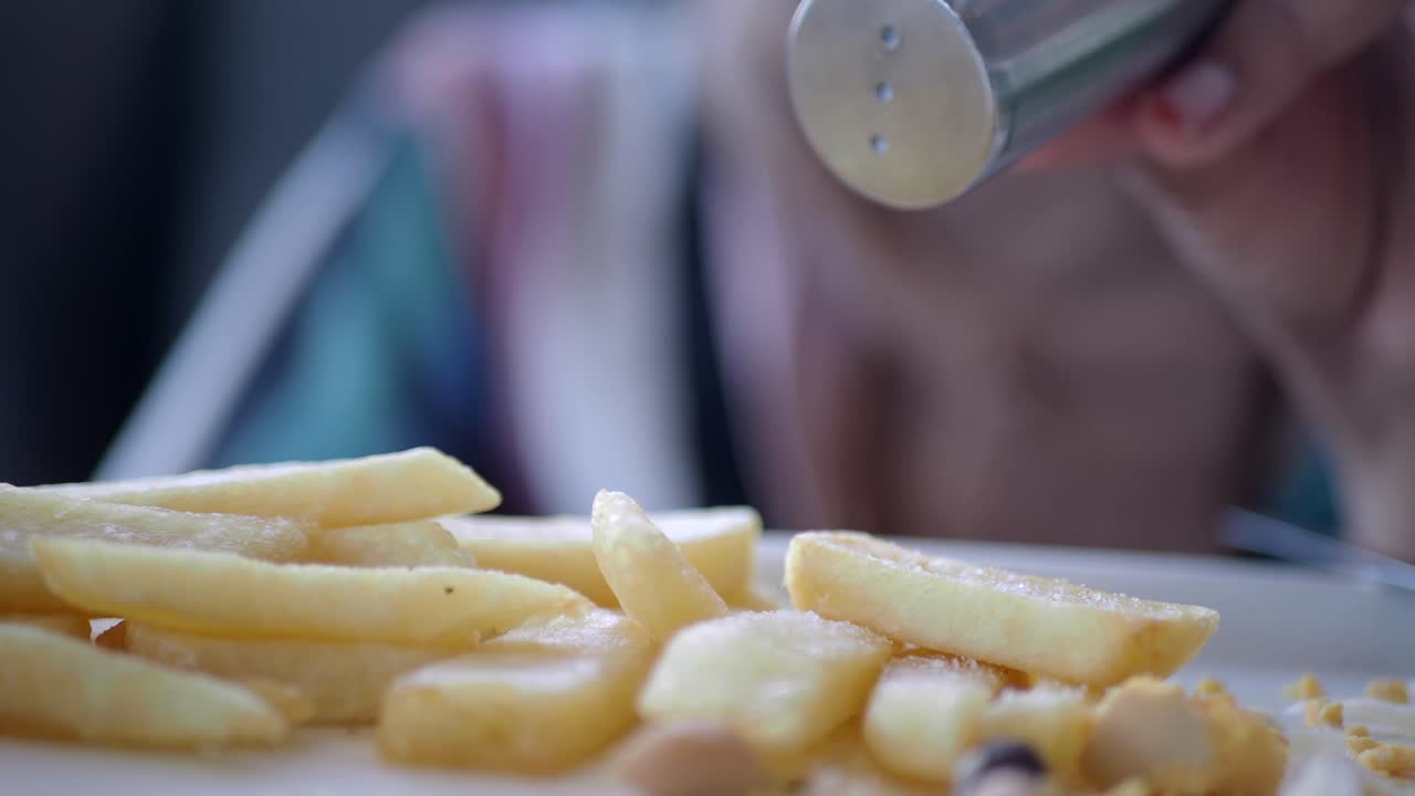 Woman Seasoning French Fries with Salt and Pepper