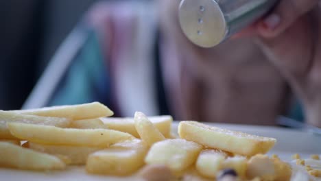 woman seasoning french fries with salt and pepper