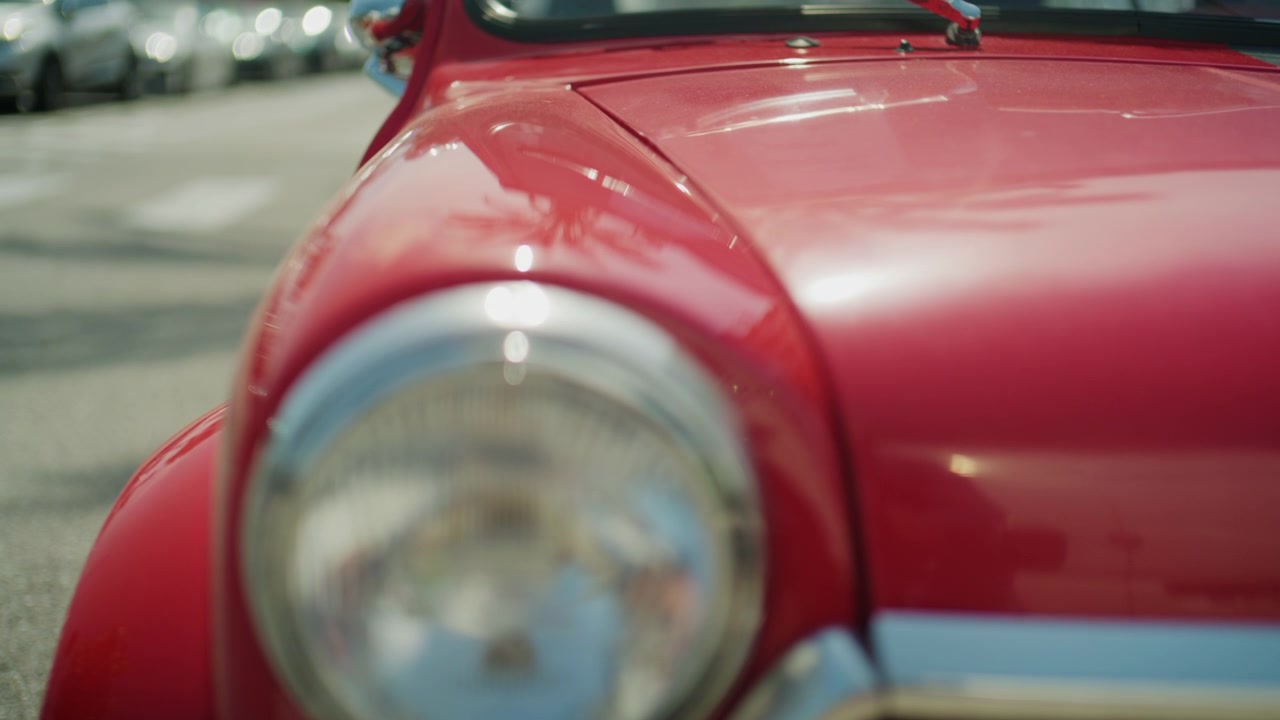 Detailliertes kinoreifes Filmmaterial eines klassischen roten Oldtimer-Automobils von außen, mit weichgezeichnetem Hintergrund und polierten Retro-Designelementen in sonniger Außenumgebung