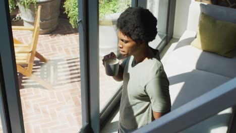 Afroamerikanischer-Mann,-Der-Zum-Fenster-Schaut-Und-Zu-Hause-Kaffee-Trinkt