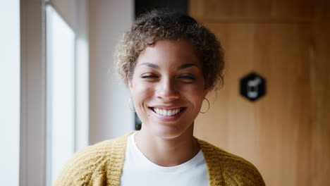 young mixed race woman standing by the window in an office laughing, head and shoulders, close up