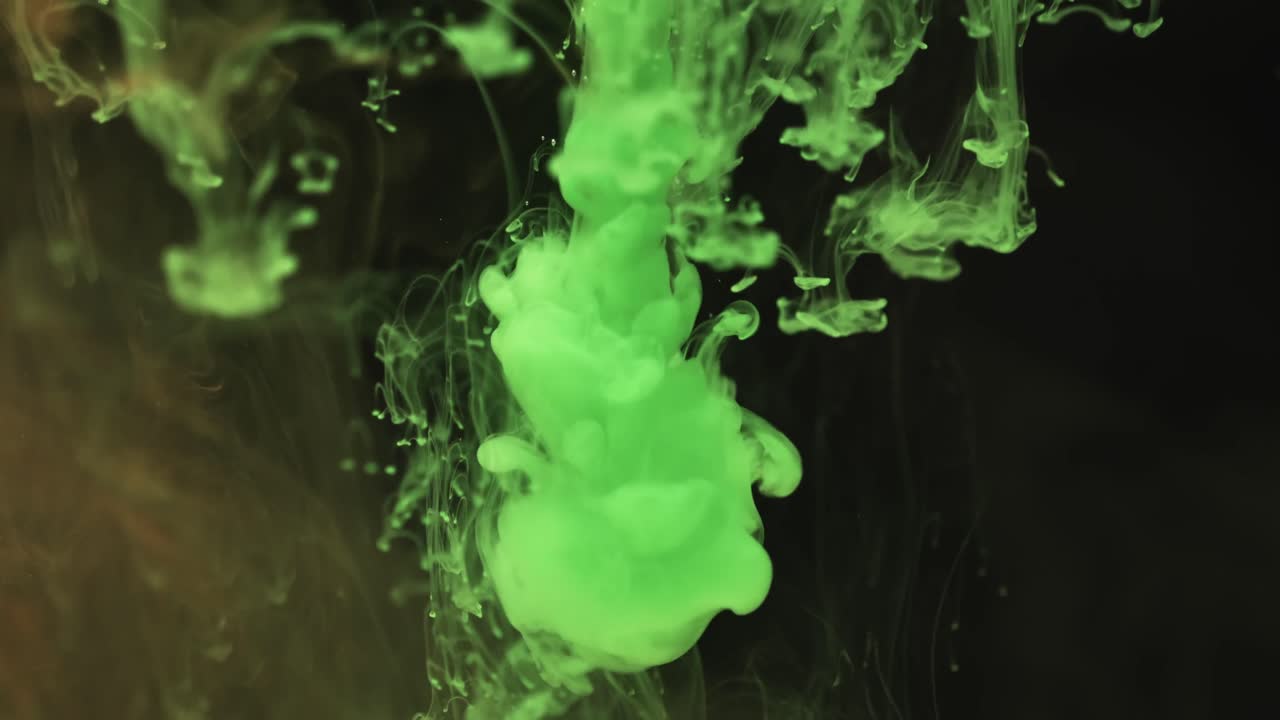 Slow motion video of green watercolor ink mixing in water against black background