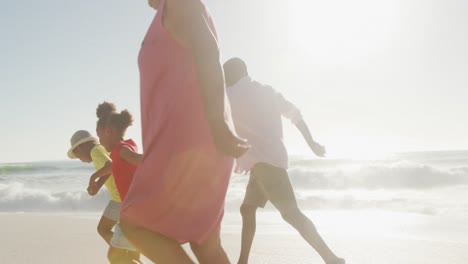 smiling senior african american couple running with grandchildren on sunny beach