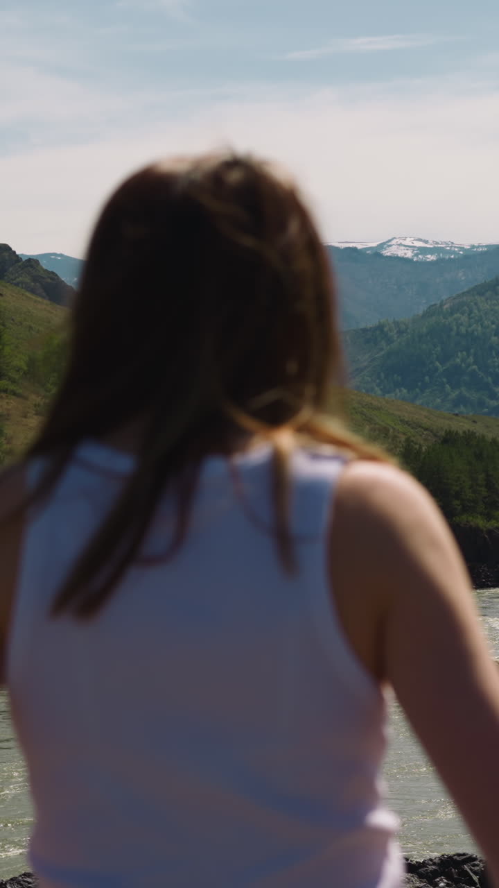 River runs across mountain valley and woman tourist on sunny day backside view. Wild environment of hillside in windy weather. Wanderlust lifestyle