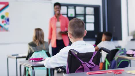 Caucasian-schoolboy-sitting-in-wheelchair-with-diverse-schoolchildren-and-teacher,-slow-motion