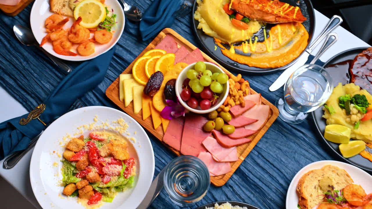 Vista dall'alto di una tavola festiva imbandita. Selezione di antipasti e piatti principali, inclusi tagliere di salumi, frutti di mare e verdure, su un tavolo
