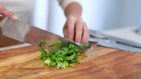 close-up of hands chopping fresh coriander on a wooden board in a bright kitchen setting