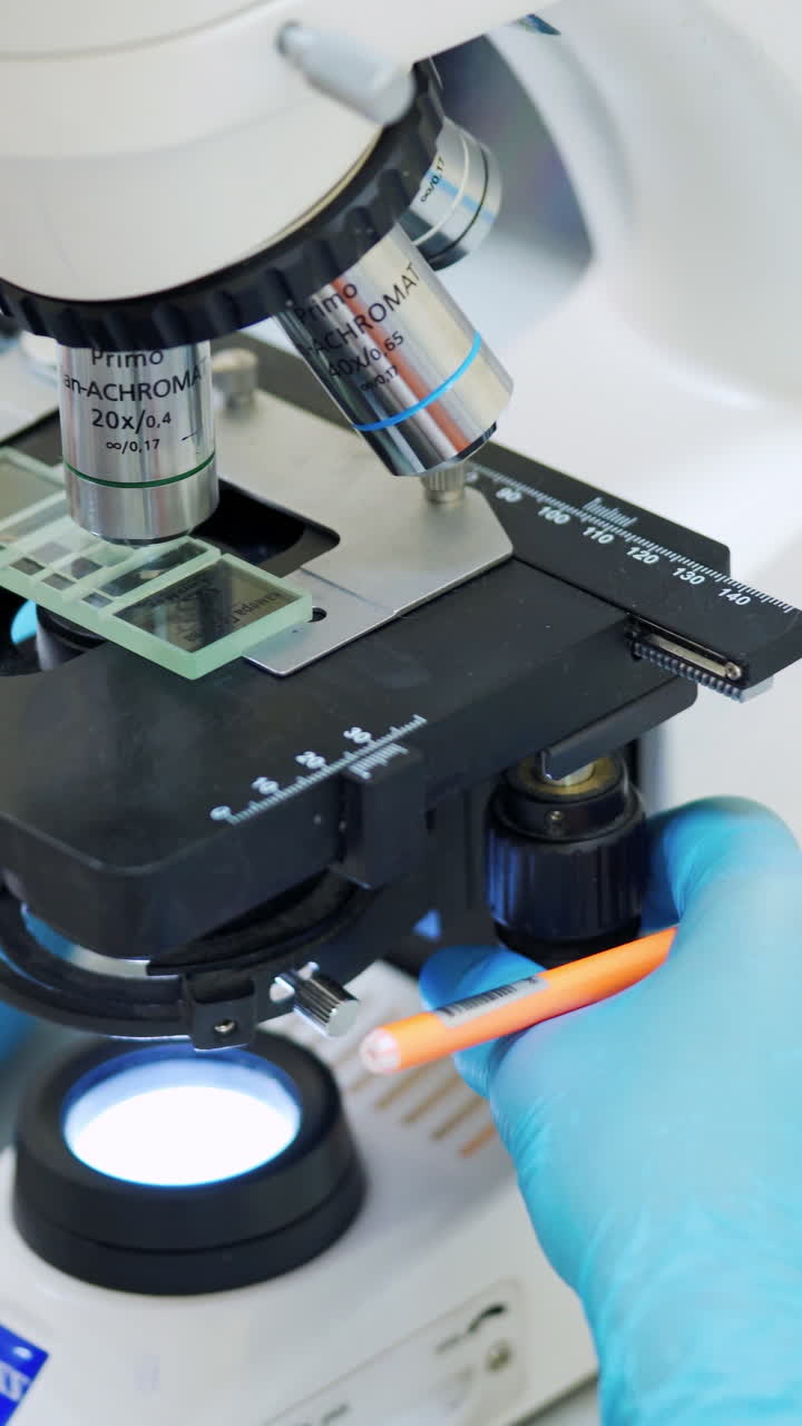 Laboratory examination of blood. Close up of female scientist in uniform working with microscope in the laboratory. Vertical video