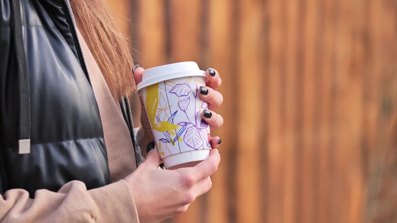 Elegante tazza di caffè usa e getta con motivi a foglie tenuta da una donna in una scena autunnale