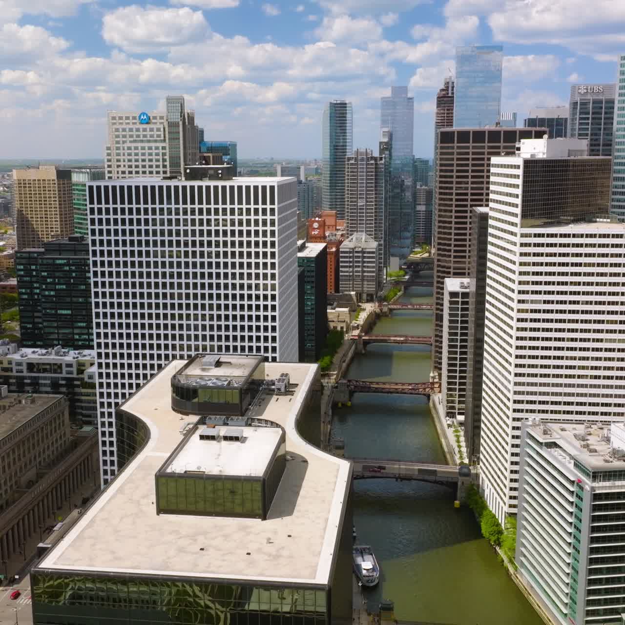 Chicago River with multiple bridges over and yachts sailing along. Drone footage over the waterway among beautiful buildings