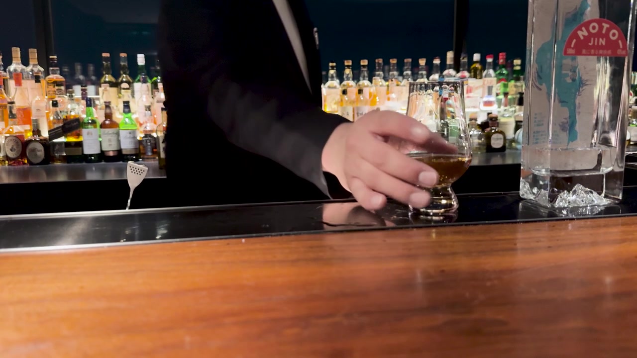 En professionel bartender serverer et glas whisky på en trædisk i Kanazawa.