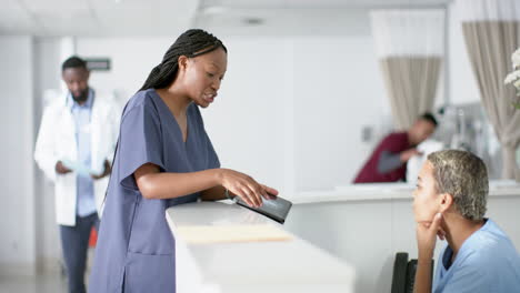 Diverse-female-doctors-discussing-work,-using-tablet-at-reception-desk-at-hospital,-slow-motion