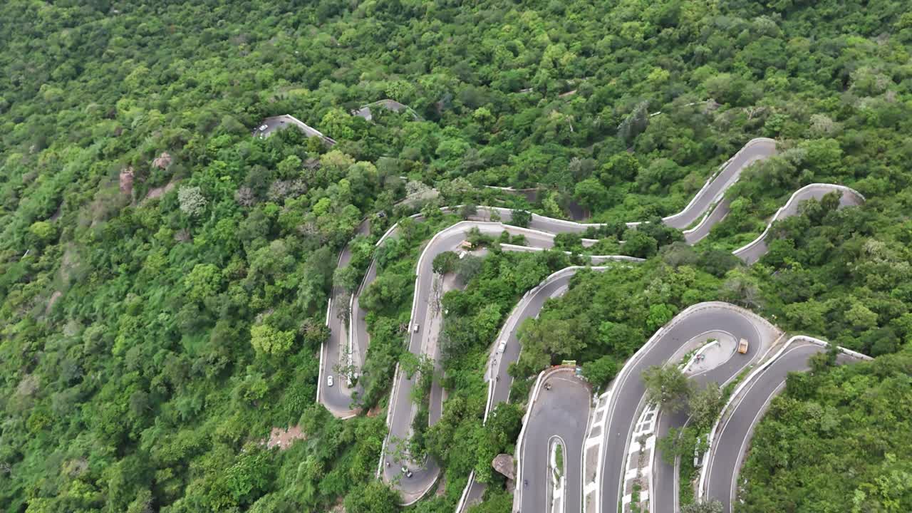 Kolli Malai, Tamil Nadu. The thrilling 70 hairpin bends are seen ascending a lush, green mountain under a bright sky. Captures the iconic road infrastructure