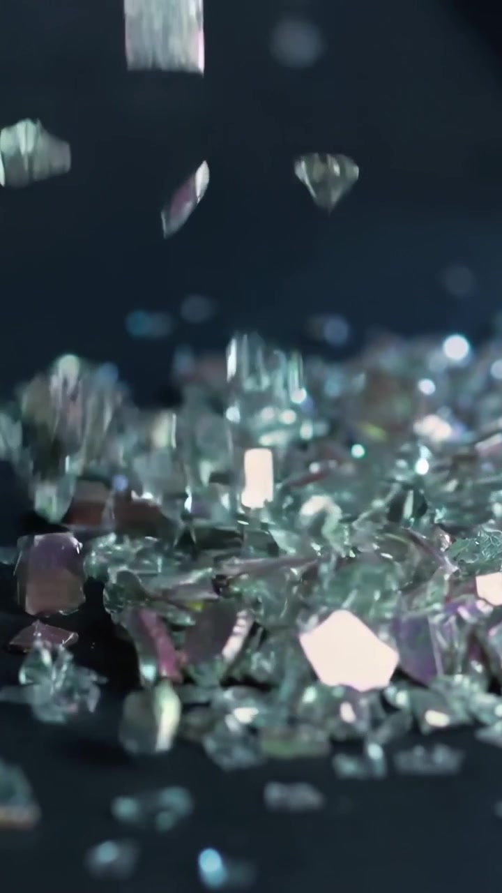 Vertical video: Dropping iridescent glass fragments forming denser pile on dark table, shimmering