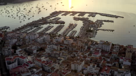 AERIAL:-Port-on-Tropical-Island-with-Boats-and-Ocean-at-Small-Town-at-Sunrise-with-Mountains-in-Background-Vacation,-Travel,-Sunset